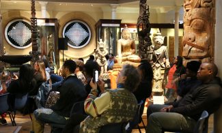 An audience seated in the museum gallery watch and listen to a musical performance. 