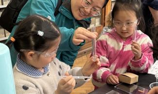 Two young visitors to the museum are wearing lab goggles and holding up test tubes. They are conducting an experiment about ocean chemistry.