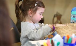 alt= "a young girl with long brown hair tied in a ponytail plays with arts and crafts supplies"