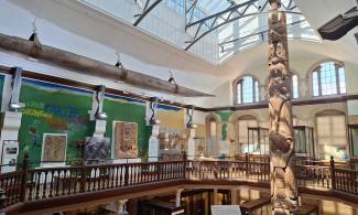 A sunlit museum gallery with a mural on its walls and a totem pole rising up from the floor below.