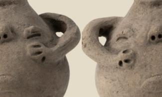 A pot with a grumpy looking face on one side with handles in the shape of arms.