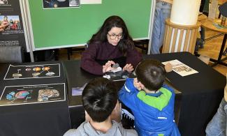 Dr Rayssa Martins-Pimentel, an Earth Scientist from the University of Cambridge Department of Earth Sciences, is showing some meteorites to two captivated young visitors to the museum. She studies the chemistry of meteorites to understand the formation of the Earth.