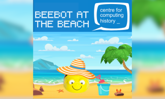 The image shows a beach and Bee-Bot with a summer's hat, bucket and spade.