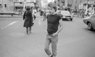 A black and white image of a man crossing a busy street.