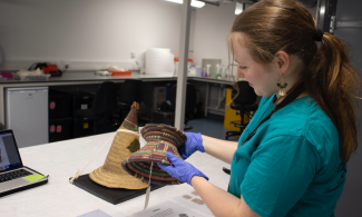 A museum intern holds up a coffee pot holder made from basketry inside the workroom of the off-site store..