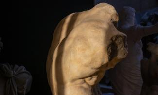 An image of a sculpture of a torso with stark light and shade cast over it.
