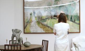 A person looking at a large landscape painting in the Kettle’s Yard house, beside a wooden table displaying a sculpture.