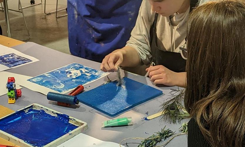 A young person sits a table and has a go at making a nature-inspired print at an Arts Pioneers session.