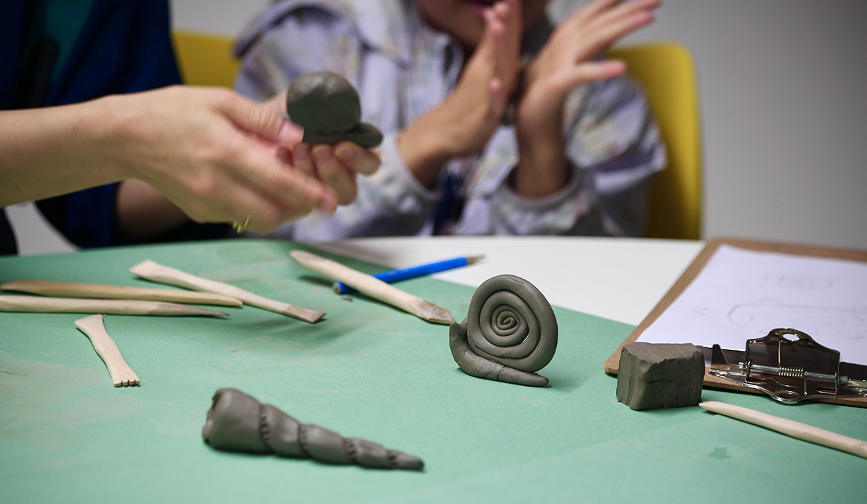 A close up of two people's hands as they form clay in their hands at a Creative Club session.