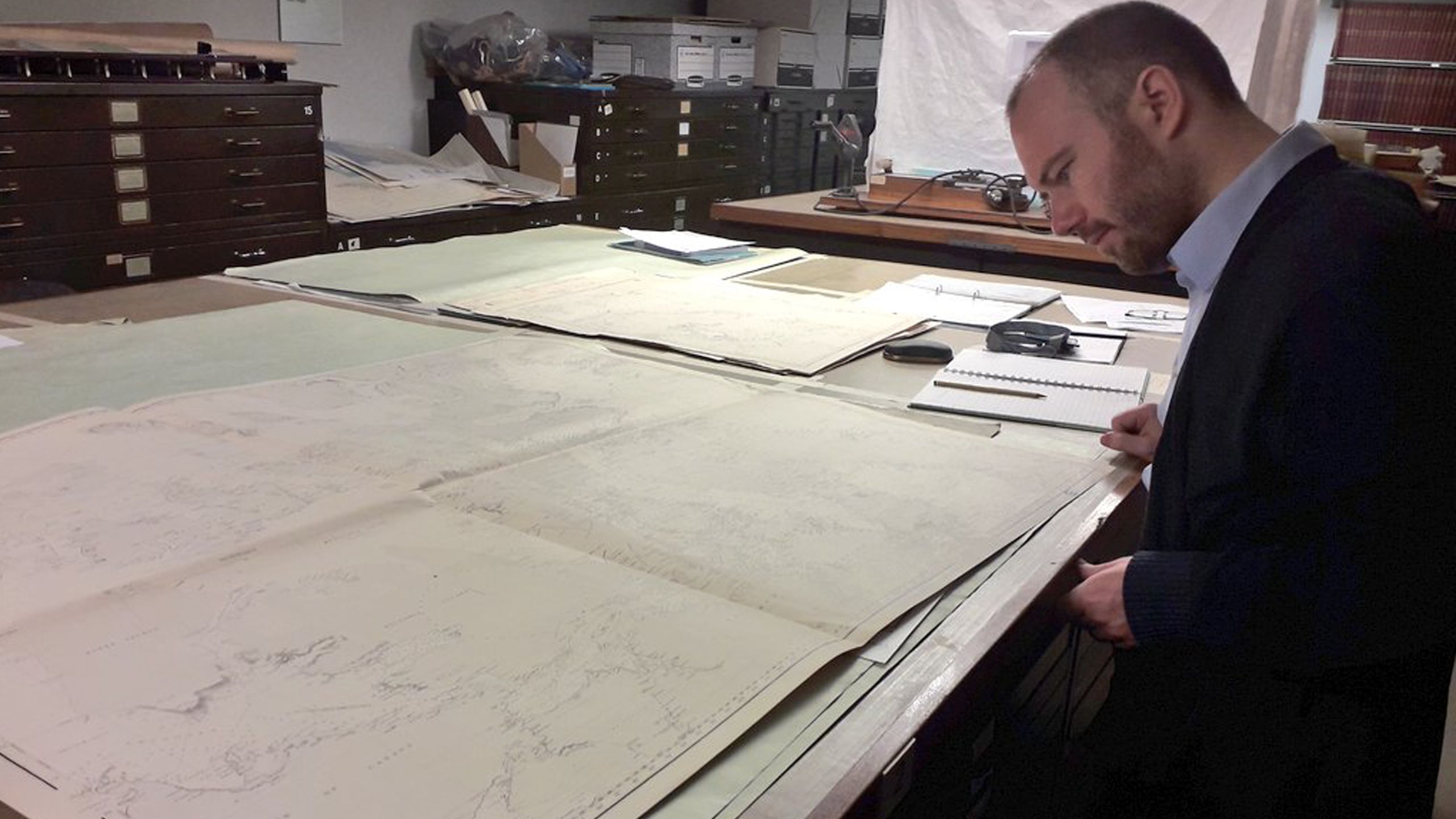 John Woitkowitz stands to the right of a large table covered in paper maps.