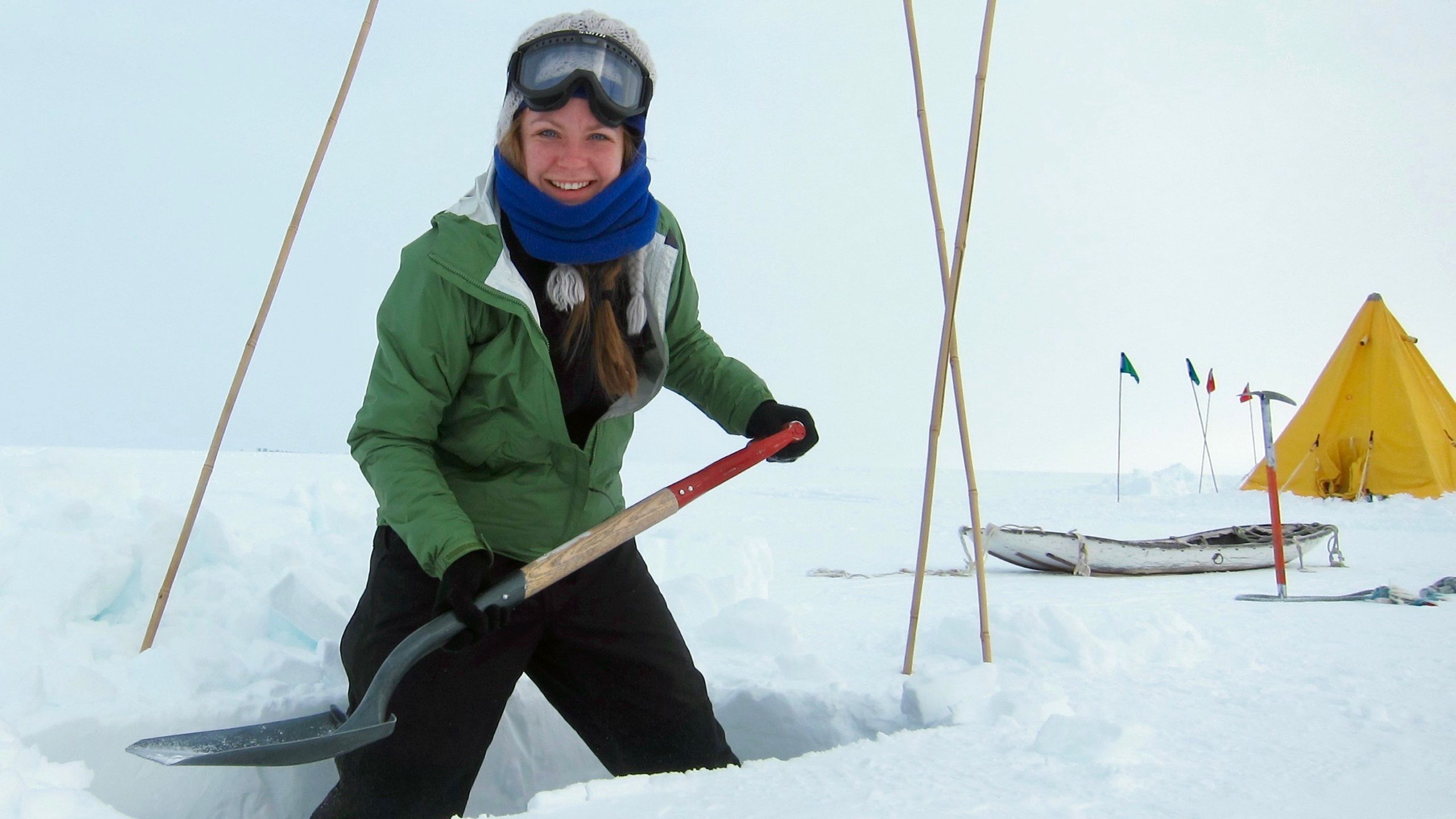 Morgan Seag digging in the snow in Antarctica. A sledge and a yellow tent are visible in the background.