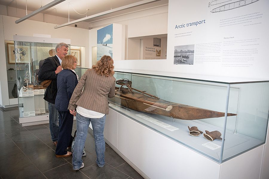 Three museum visitors look at a kayak in a showcase.