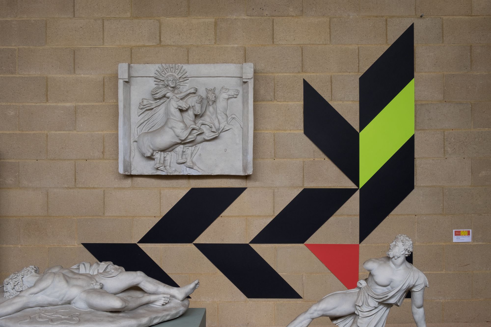 Black, red and yellow shapes angularly frame plaster casts.