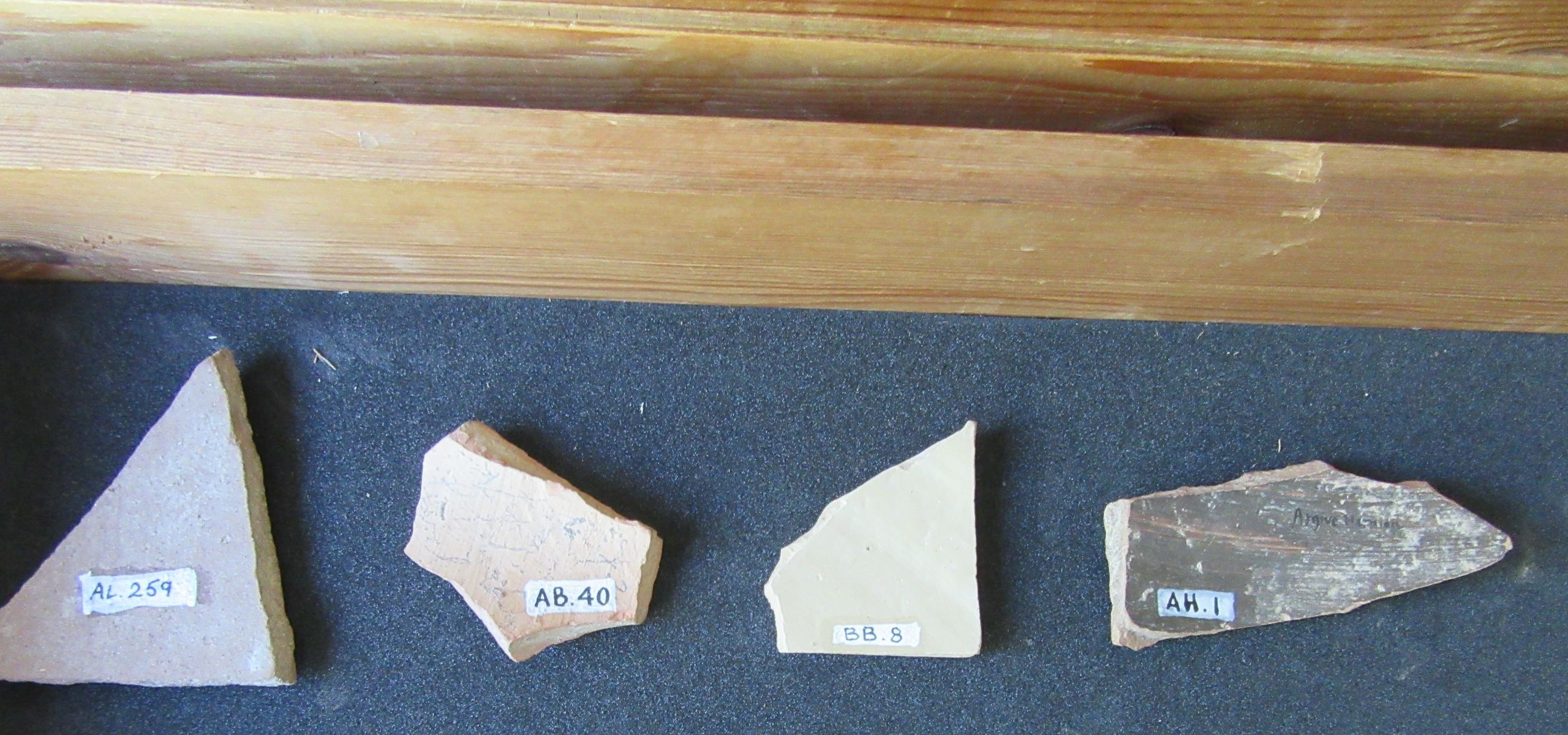 Sherds in a wooden box with their museum numbers facing upwards.