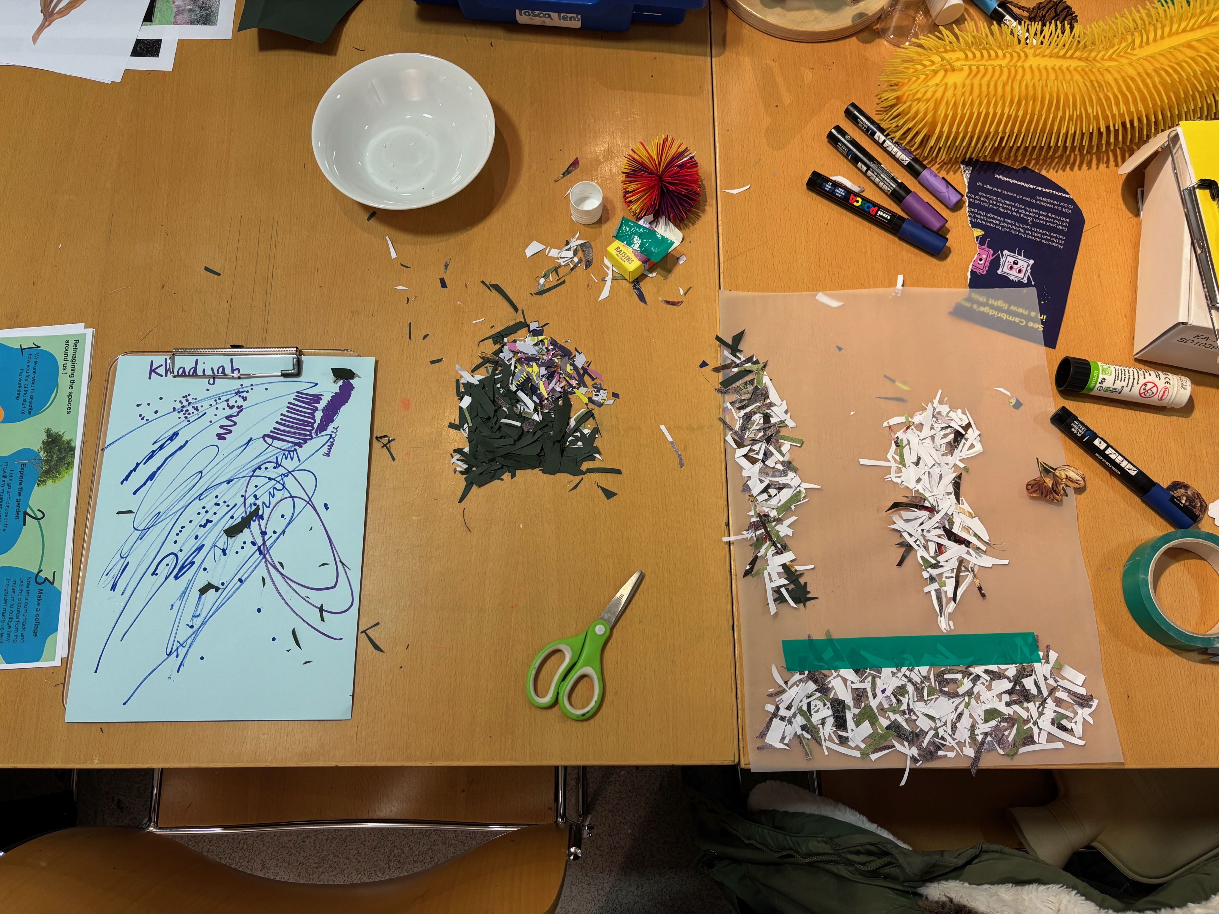 An overhead view of Khadija's space at the table, filled with craft materials, scissors, snipped bits of paper and pens.