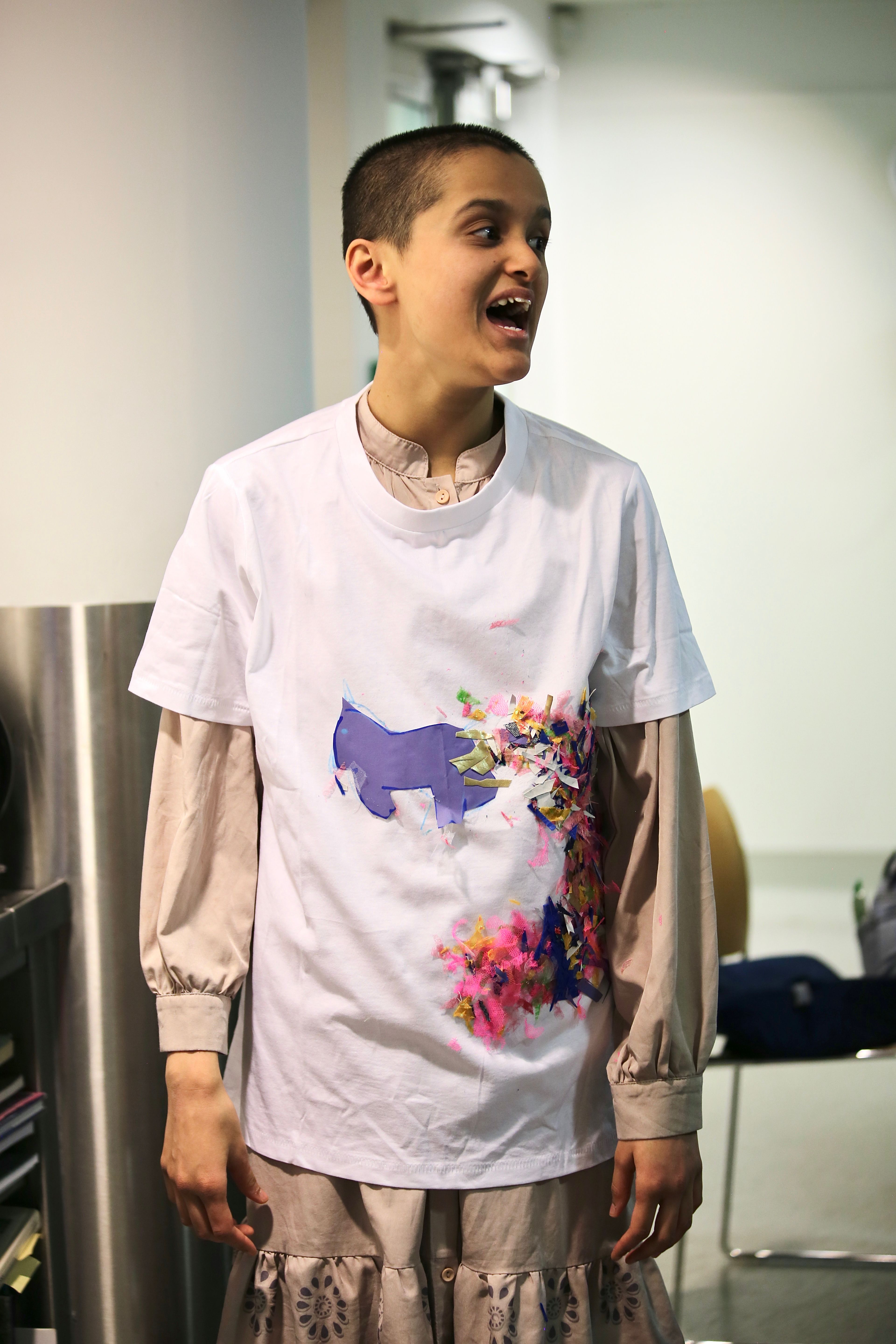 Khadija smiles and stands wearing her white t-shirt collage creation.