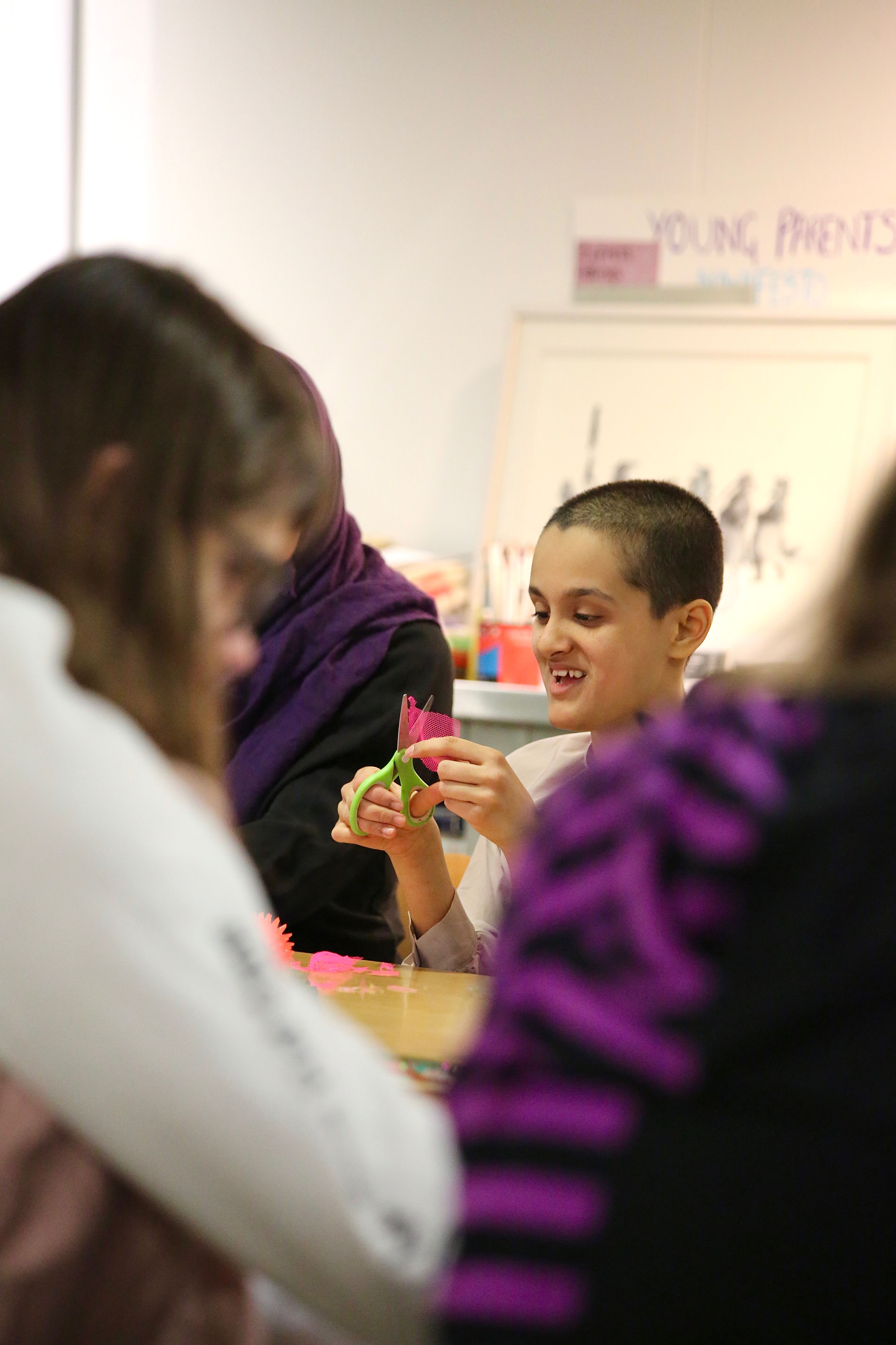 Khadija smiles and cuts up a piece of pink mesh with a pair of scissors at an Arts Pioneers session.