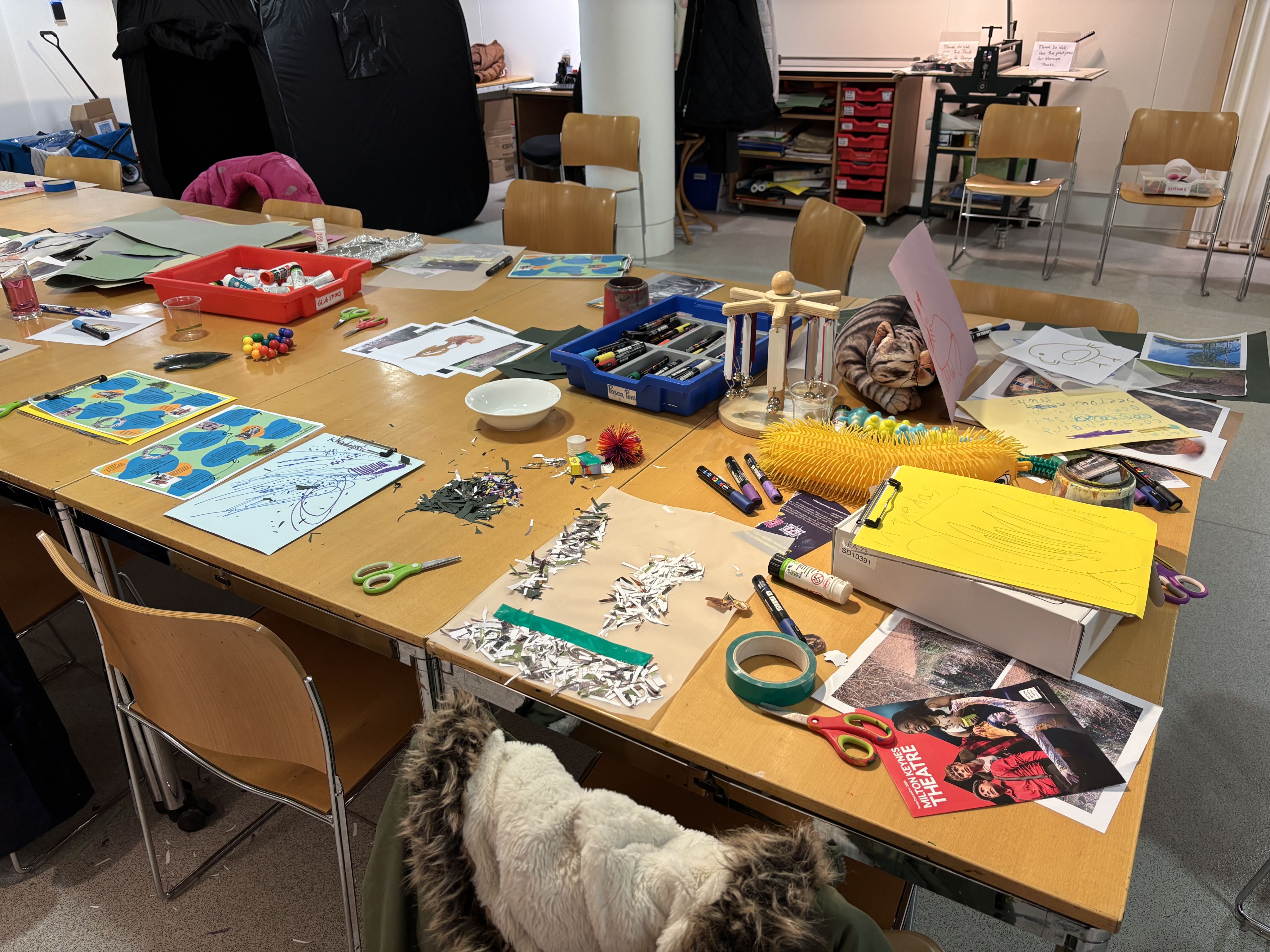 A wooden table filled with craft materials, including scissors, papers, glues and sensory toys.