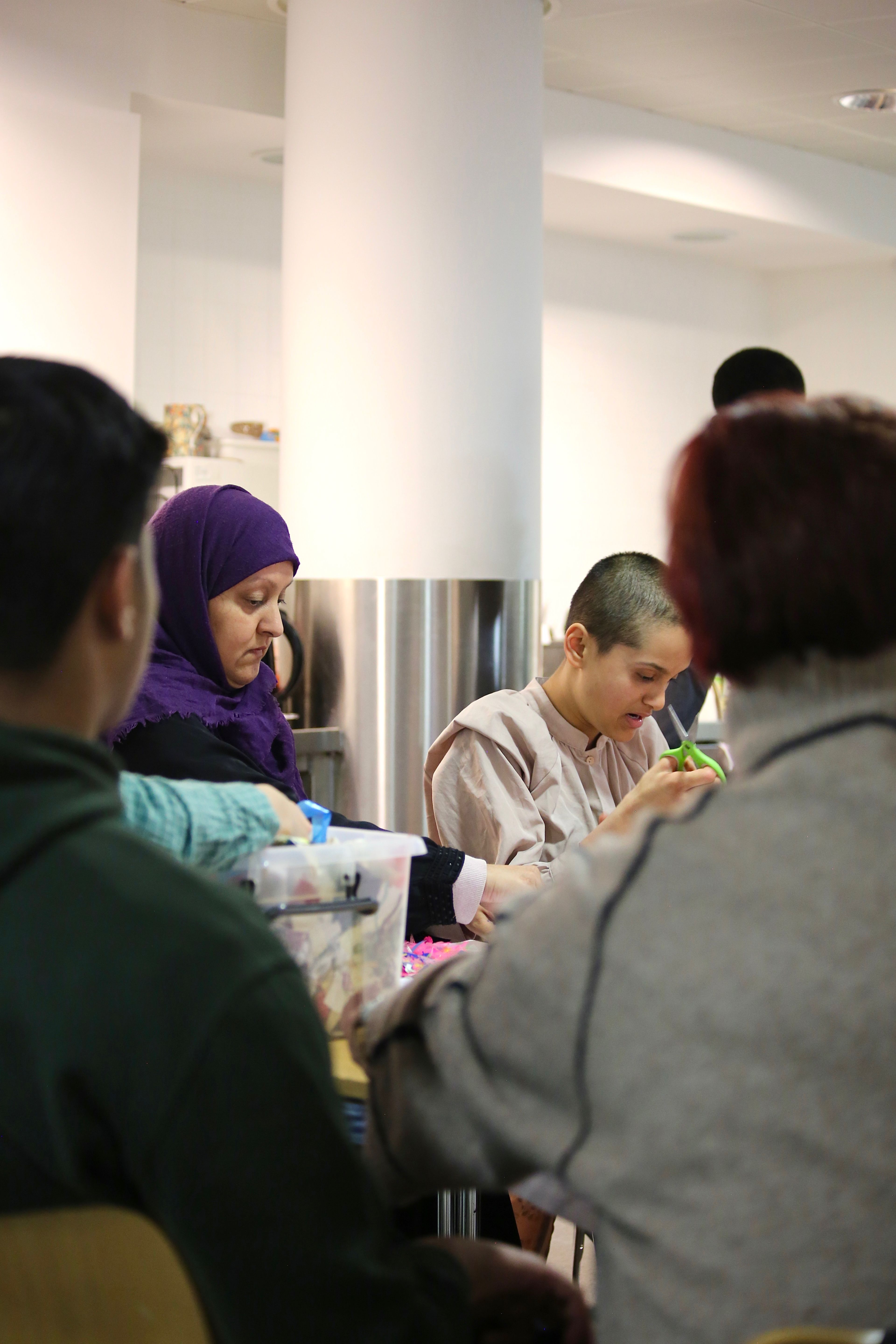 Khadija sits next to her mother Sima, wearing a purple headscarf, at a table both taking part in craft activities at Arts Pioneers.