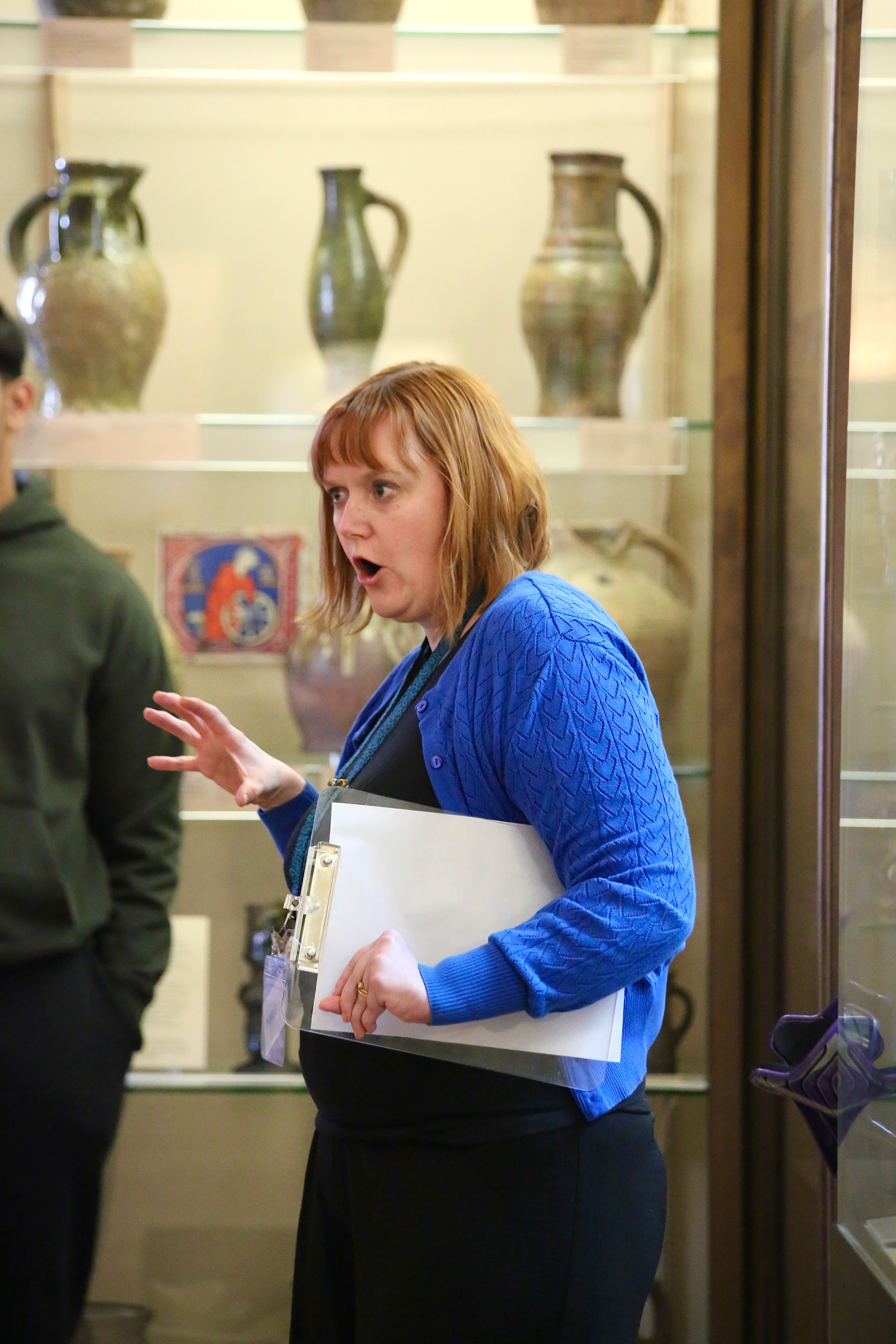 Marie Kennedy, a white woman with short red hair and a blue cardigan, animatedly speaks to participants at an Arts Pioneers session.