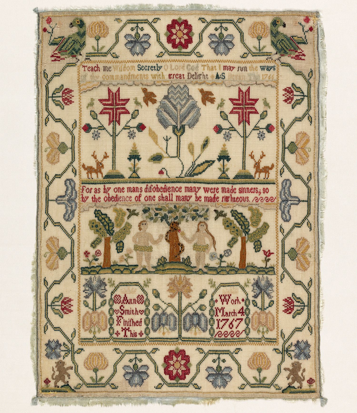 Canvas sampler, zoomed in one one piece, with the Garden of Eden and Adam and Eve picking fruit from a tree. The canvas is a light cream. It reads: 'for as by one mans disobedience many were made sinners; so by the obedience of one shall many be made righteous'. The outside decoration is very rural, trees and animals, in relatively natural colours of greens, blues and browns. The text is in red thread.