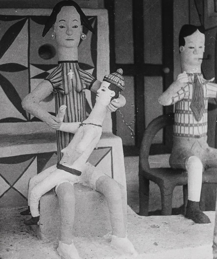 Clay woman seated on a low base holding a child across her lap; a second seated male figure appears behind her.