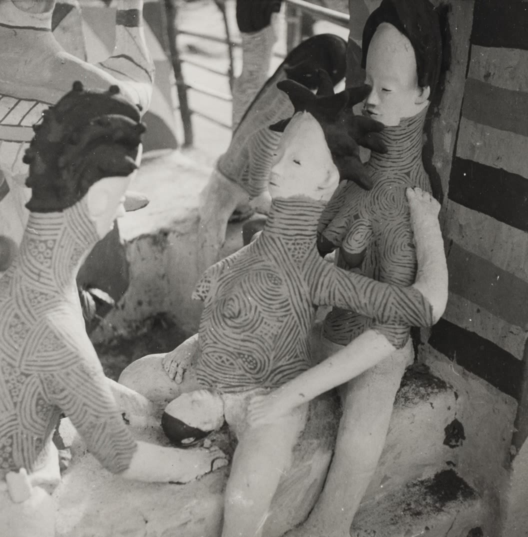 Clay figures arranged in a childbirth scene: a woman reclines with legs extended while another figure supports her from behind, and a third figure stands nearby.