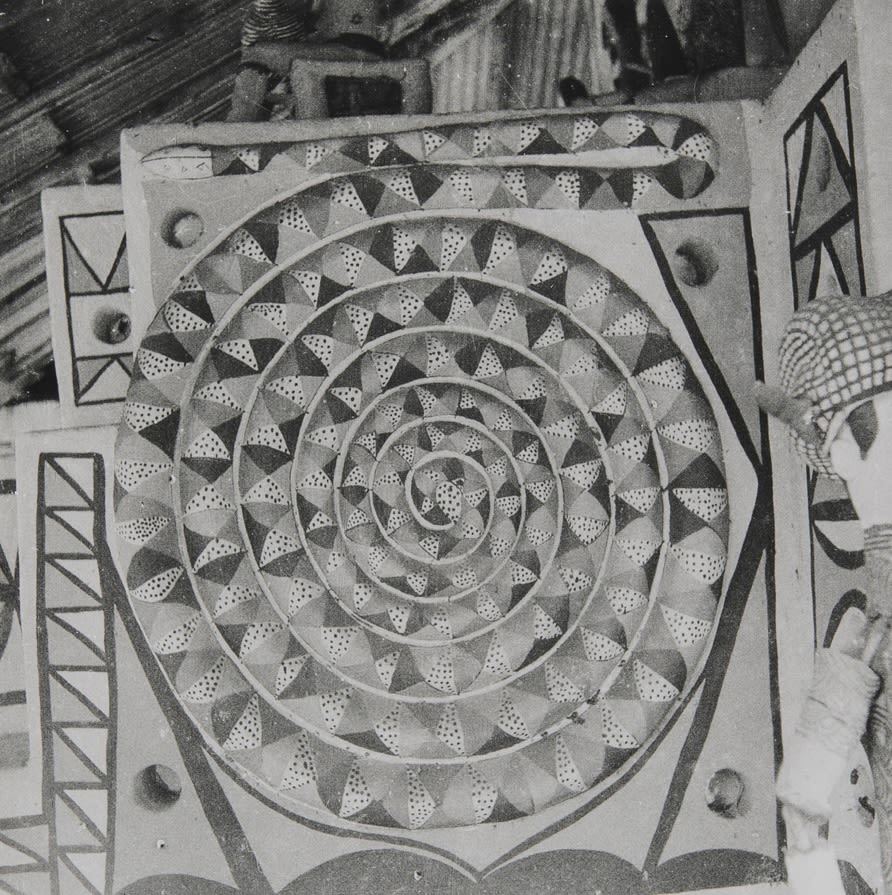 Painted wall panel featuring a large circular spiral design composed of repeated triangular and dotted motifs, framed by additional geometric patterns.