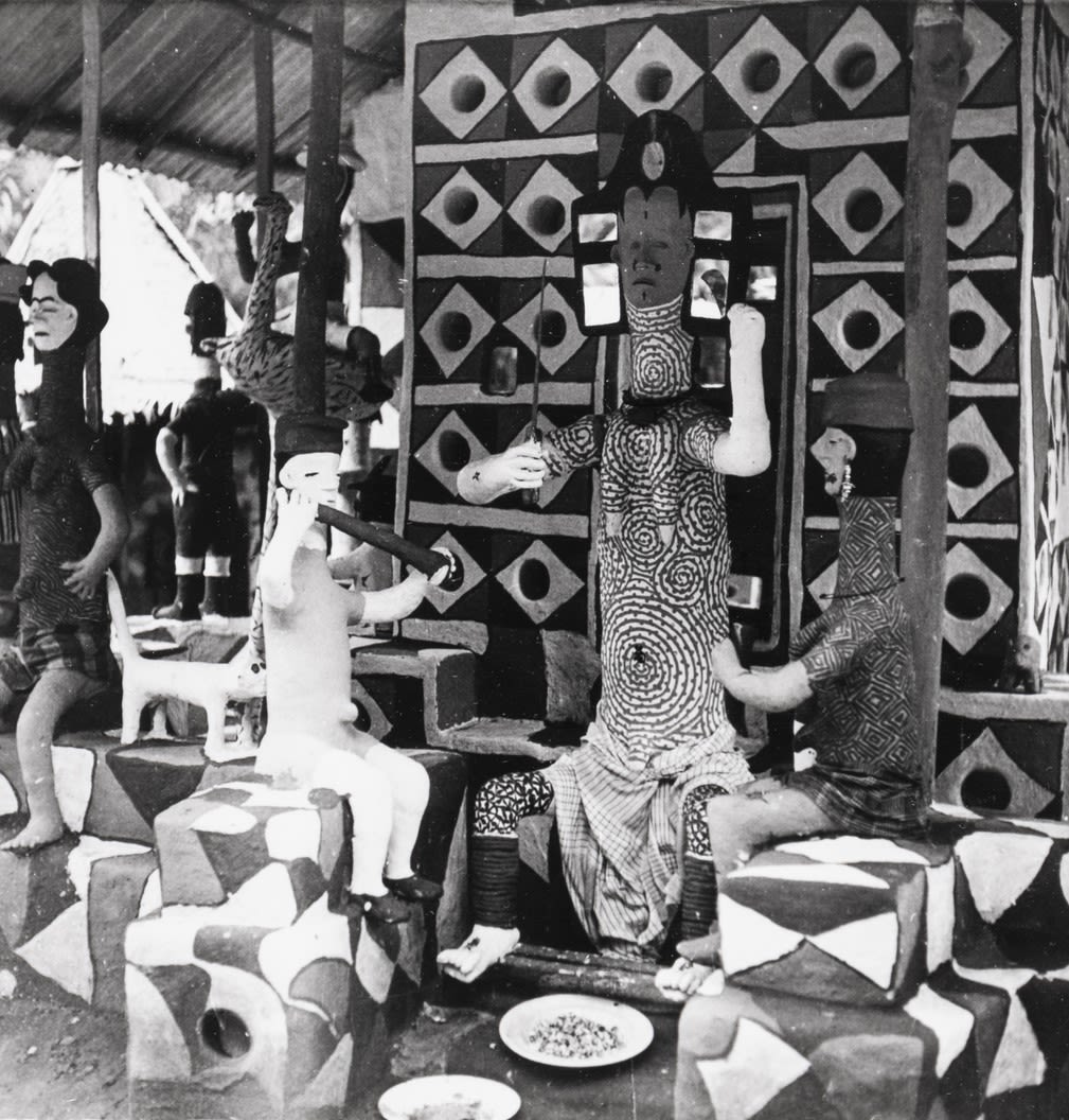 Black-and-white photograph of a painted shrine or pavilion with patterned walls and several sculpted figures seated on decorated platforms.