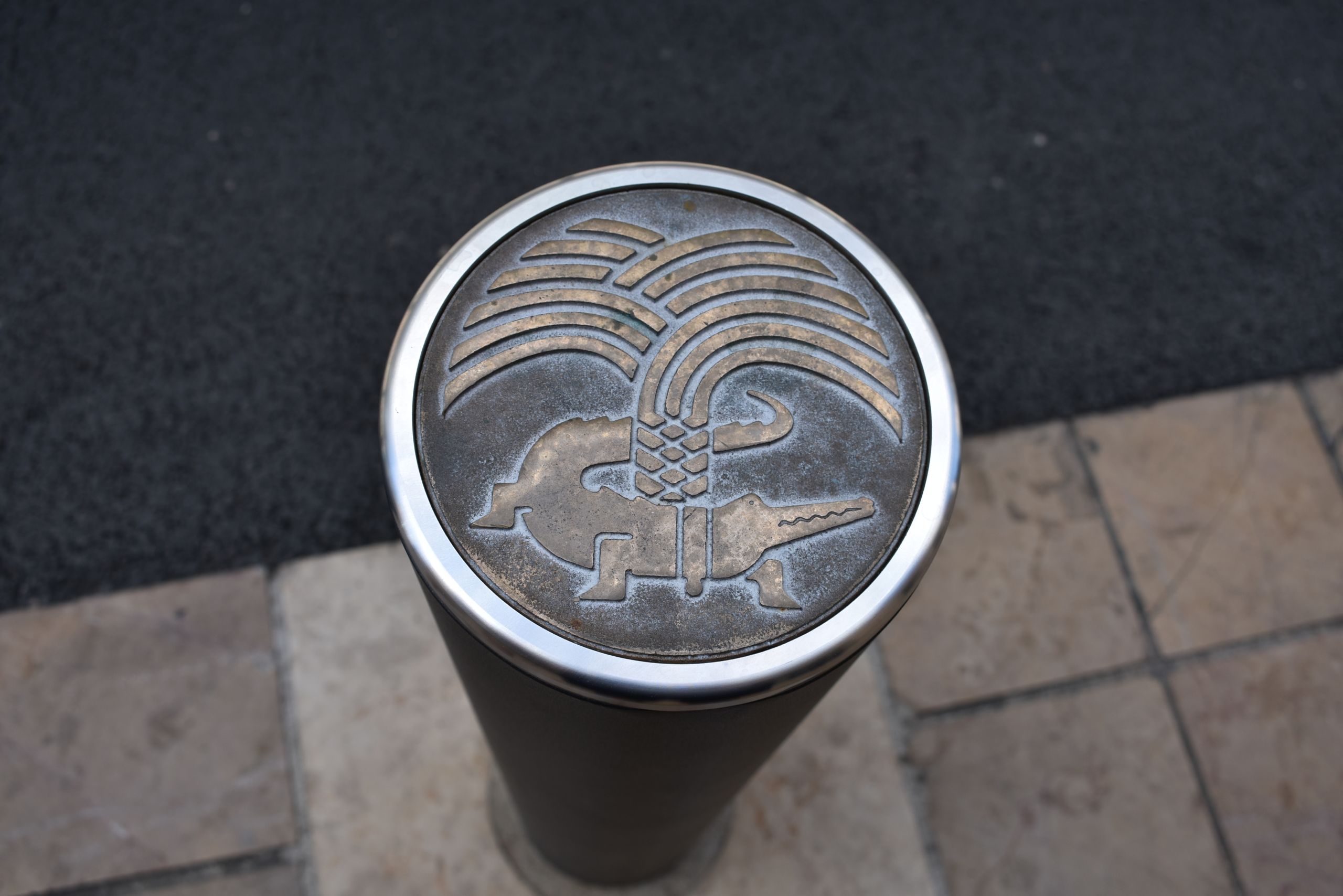 A modern bollard in with a crocodile and palm image on the top.