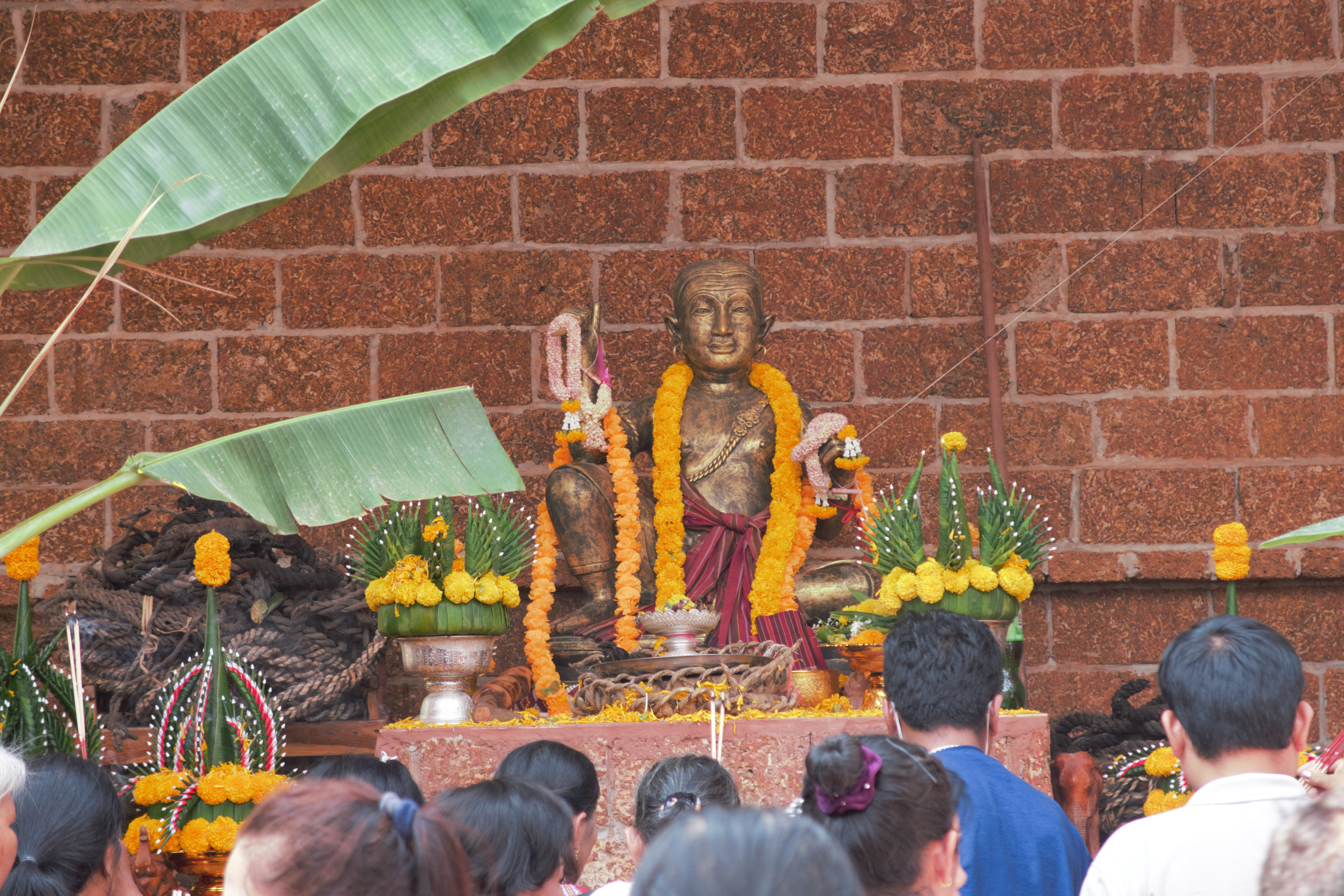 At the centre is Pakam god, a gold seated statue, surrounded by offerings. In the foreground, people can be seen worshipping the Pakam God. 