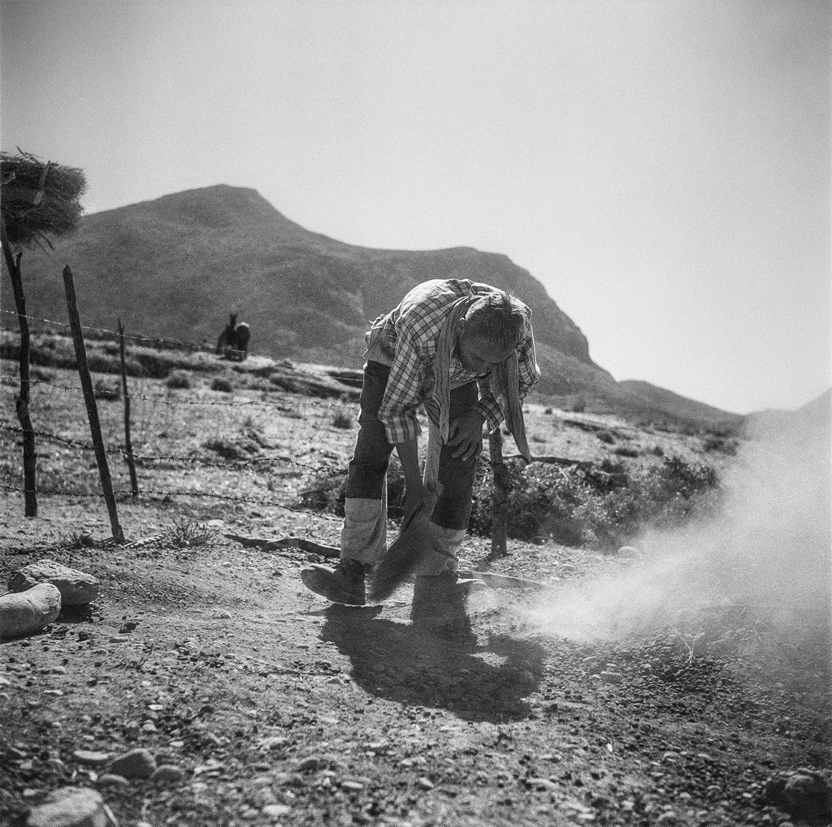 Dust rises from where a man is brushing the ground.