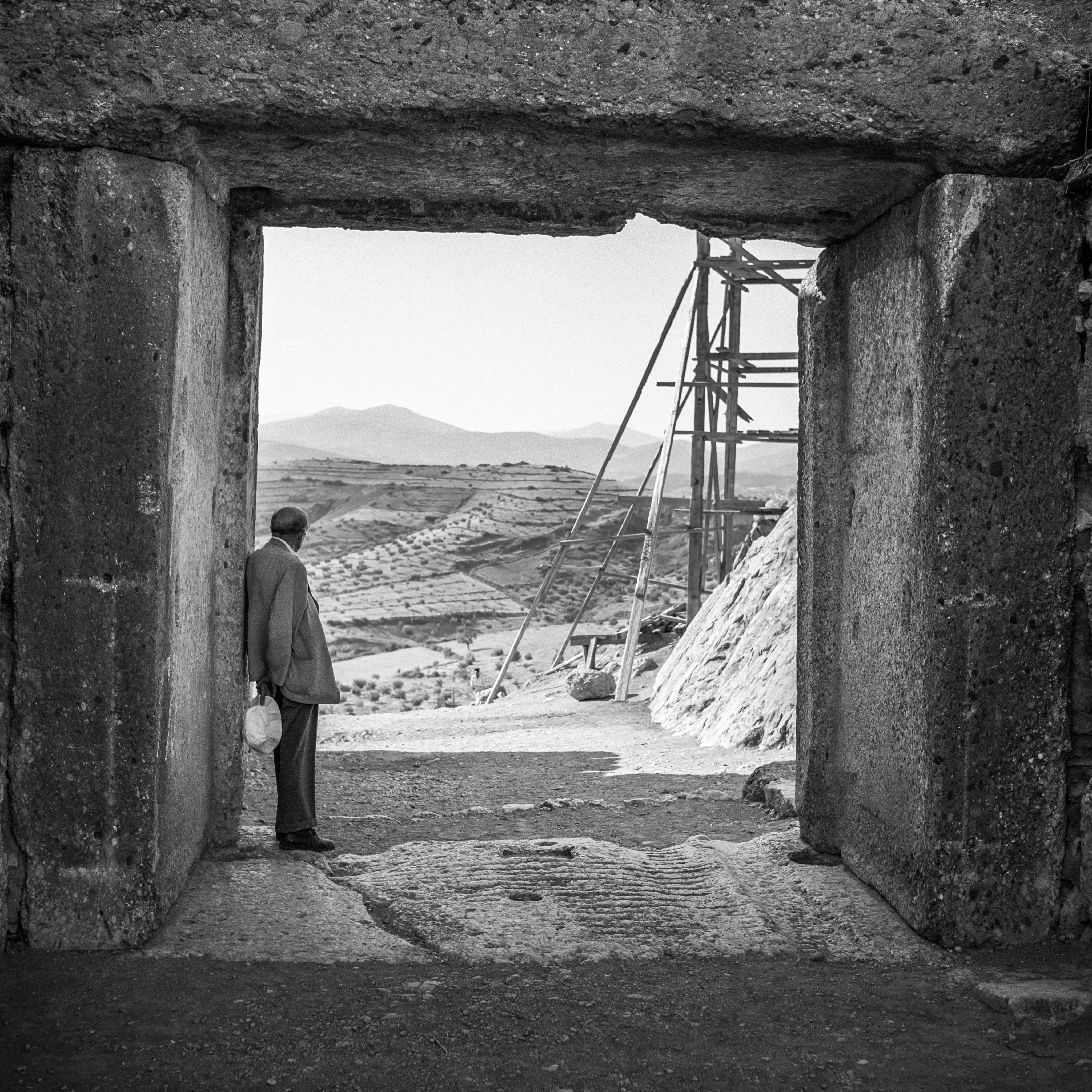 A man stands in an ancient archway, gazing out to the landscape beyond.
