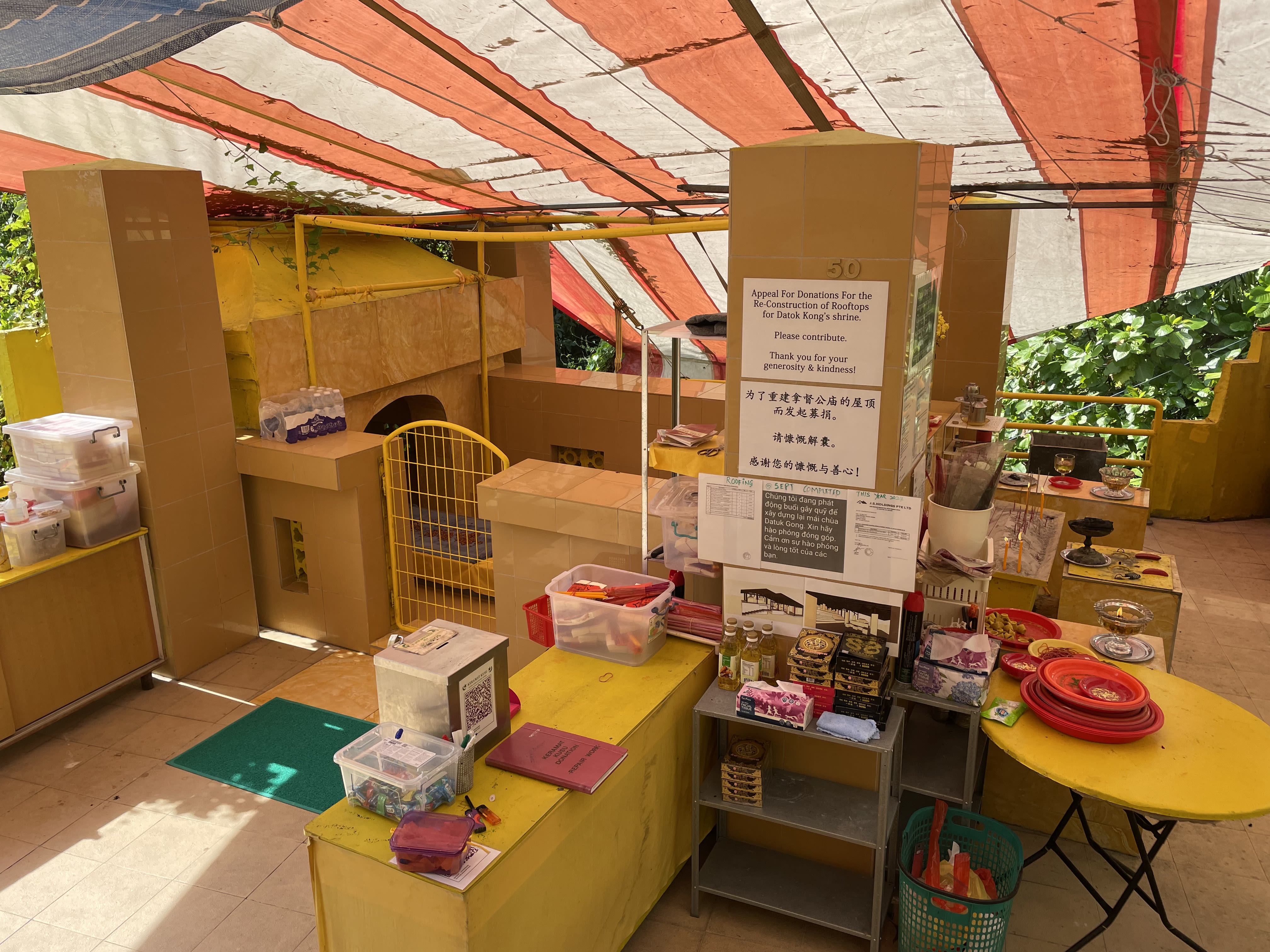Side view of a yellow shrine. On the pillars are papers printed with appeals for donations for the reconstruction of the shrine, in various languages.