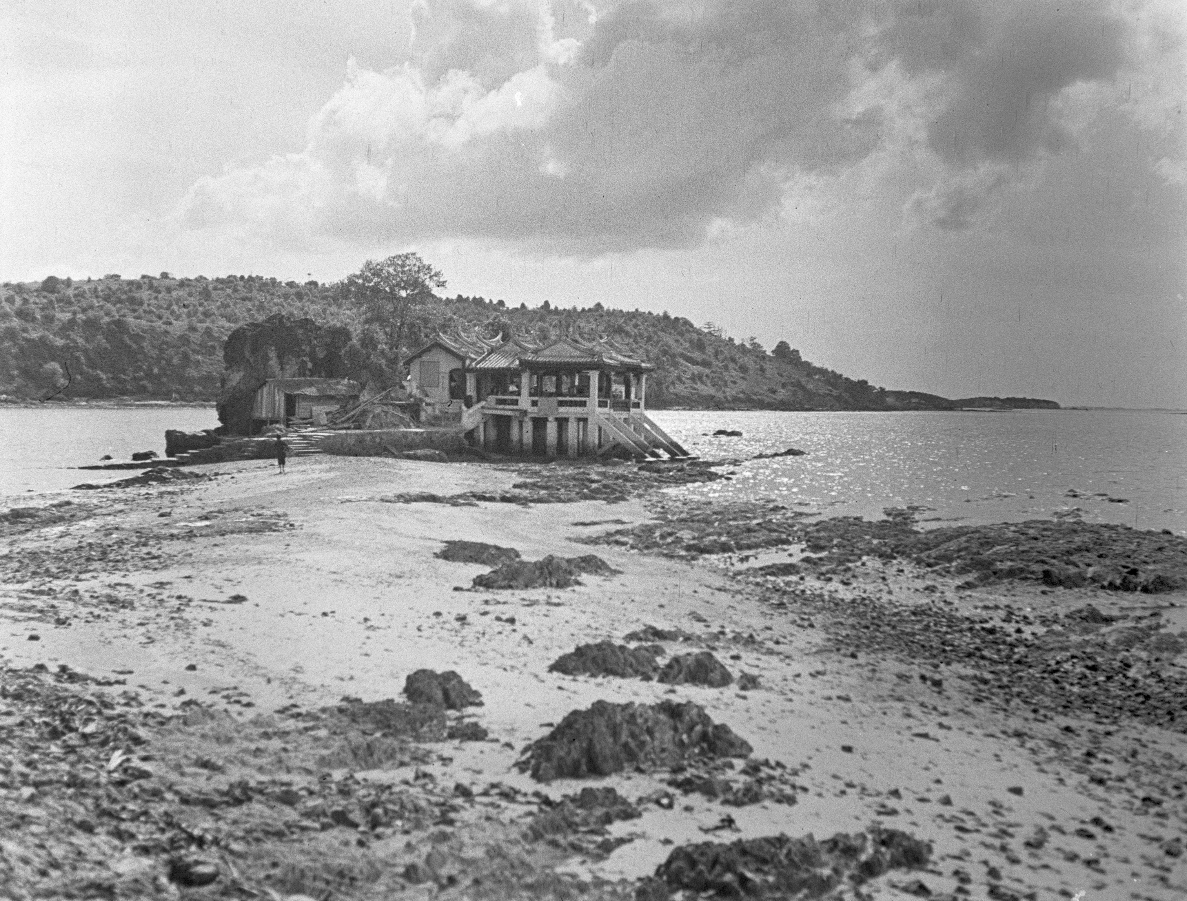 A stretch of sand with sea on either side leads to the Kusu Tua Pek Kong Temple, a building standing on stilts and with tiled roofs.