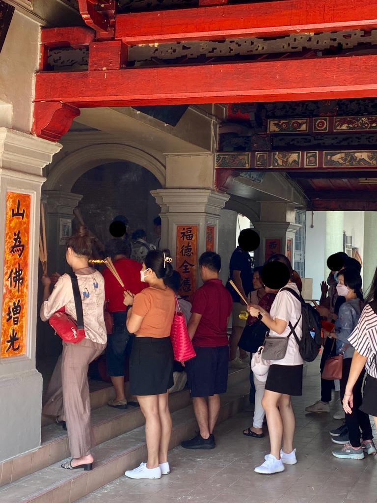 Devotees holding joss sticks stand in two lines to pray. Scrolls with Chinese characters are pasted on the pillars of this temple.
