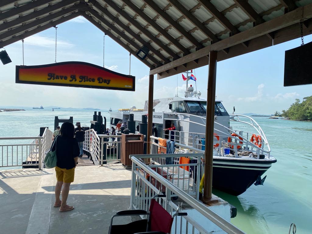 At a pier, a sign hanging from the roof reads 'Have A Nice Day'. A blue and white ferry has docked at the pier.