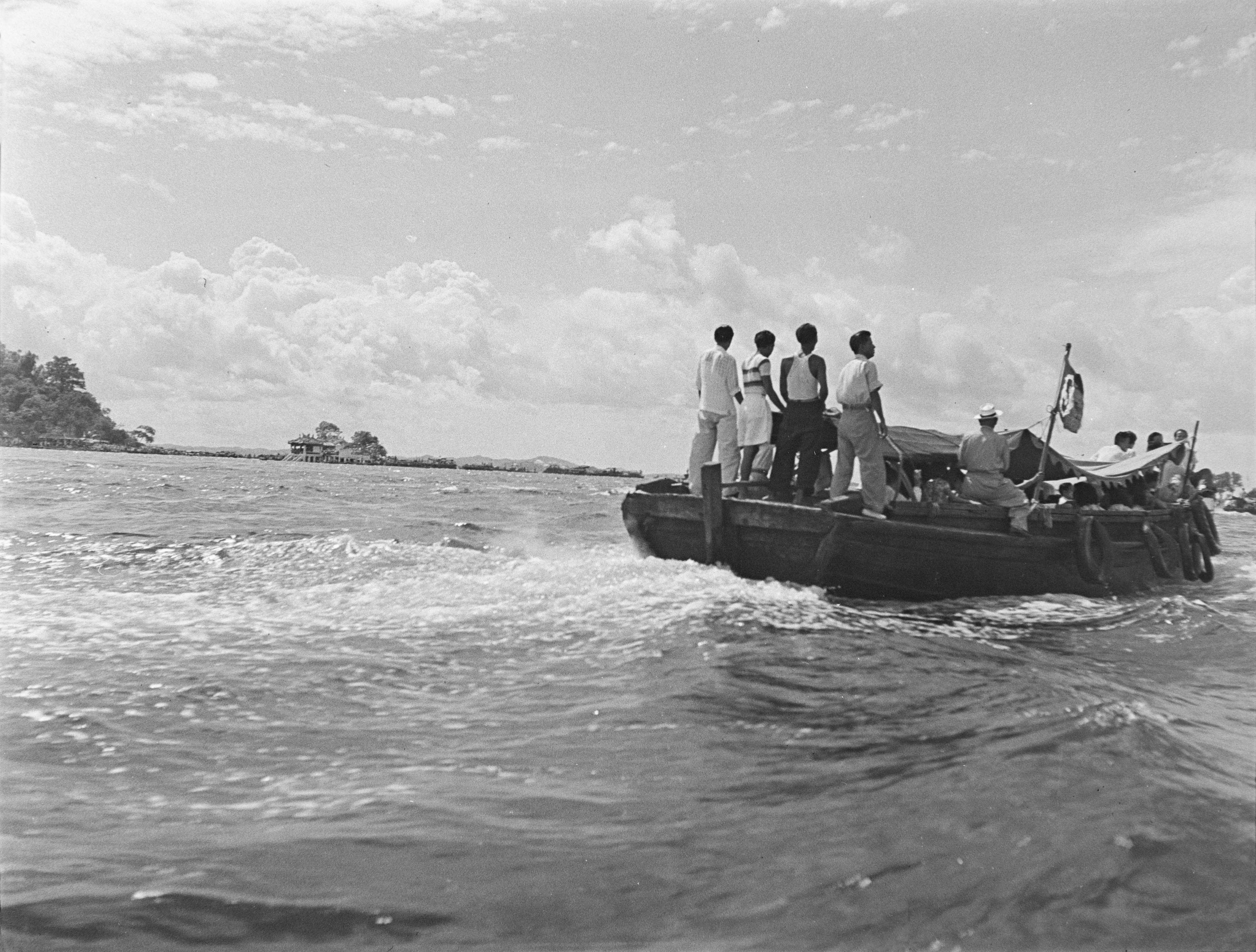 Four men stand on the stern of a boat sailing to Kusu Island, which can be seen in the background.