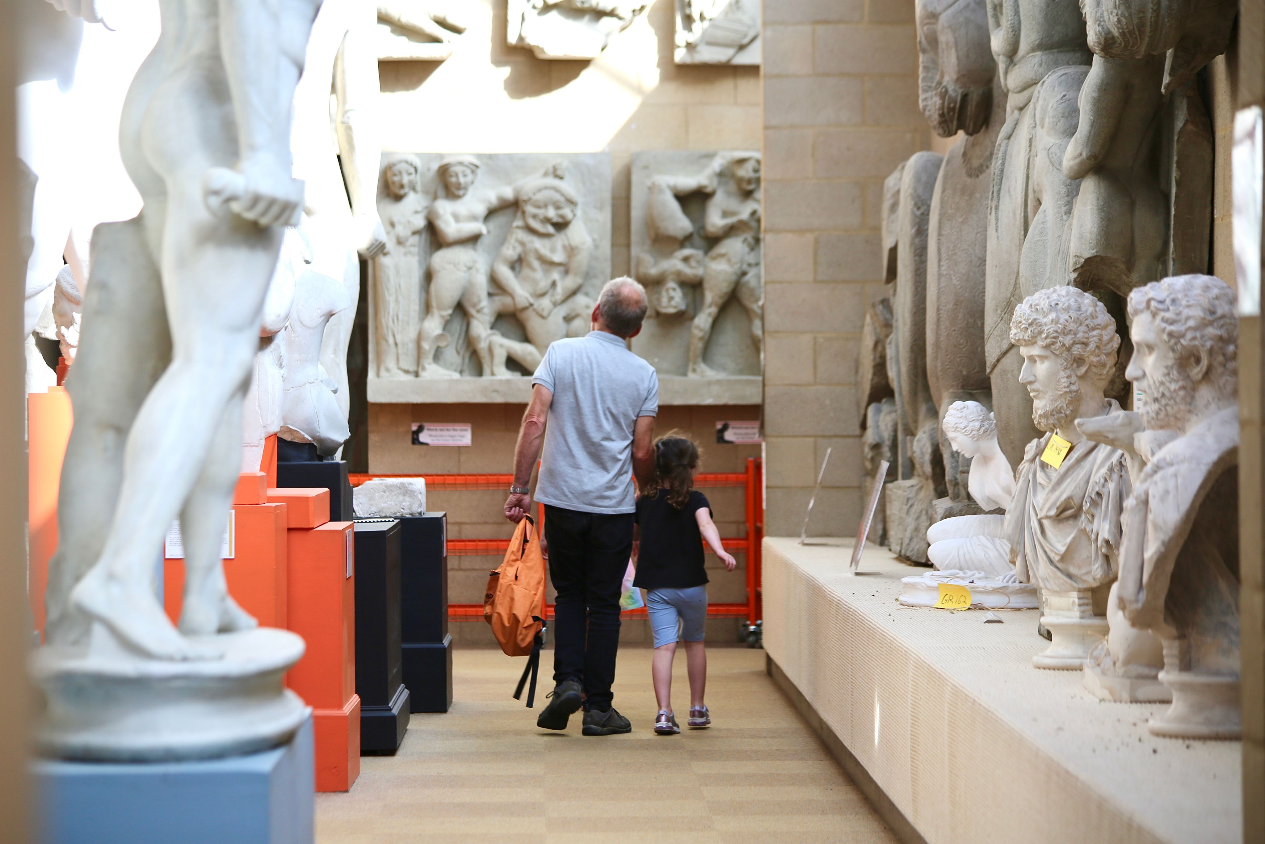A man and a young girl holding hands and walking through the Cast Gallery at the Museum of Classical Archaeology.