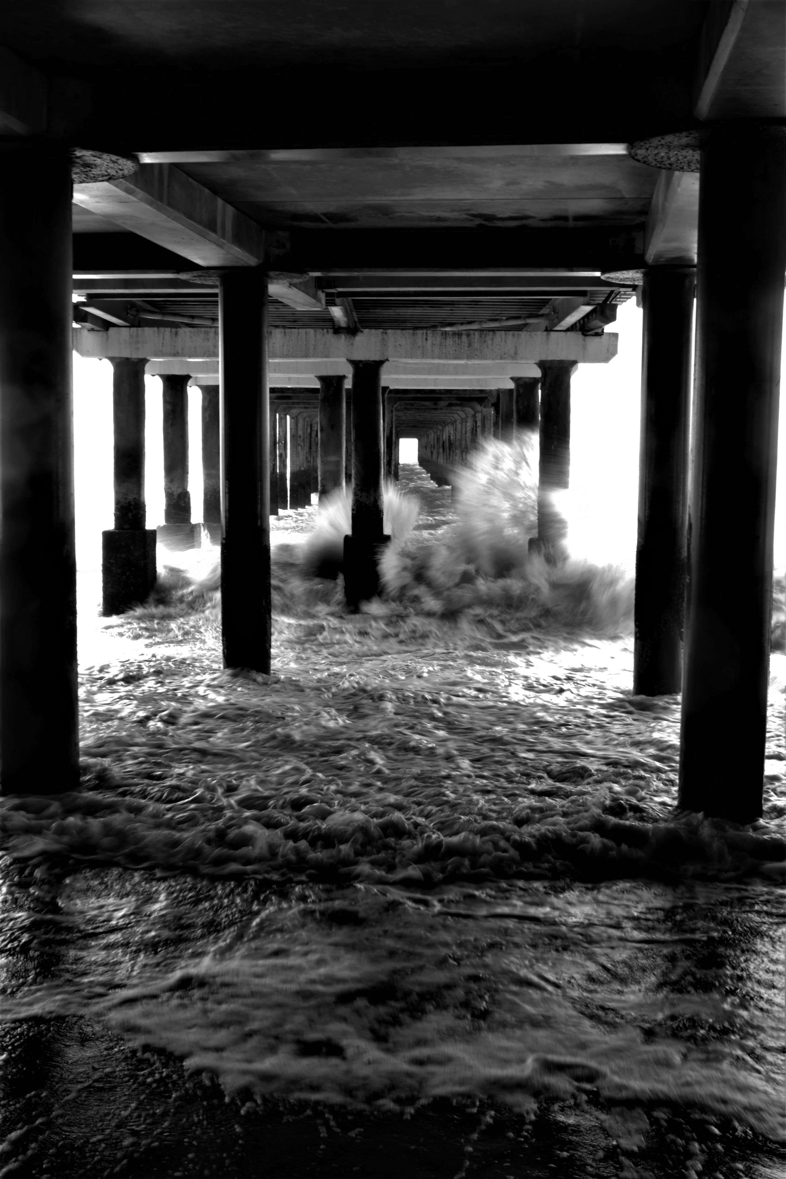 waves hitting the supports of a beach pier. greyscale. 