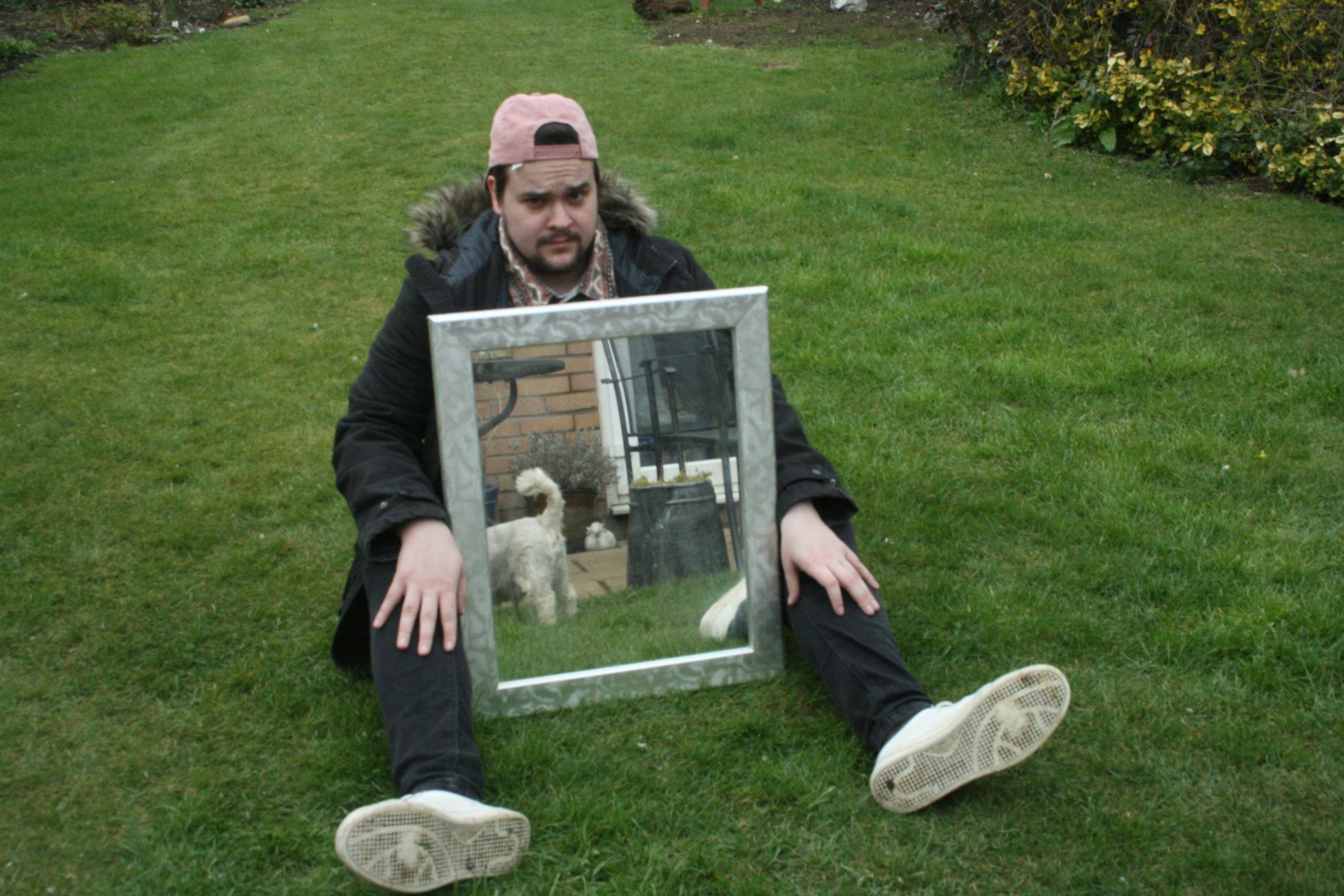 man sitting down, mirror between his legs showing a garden scene