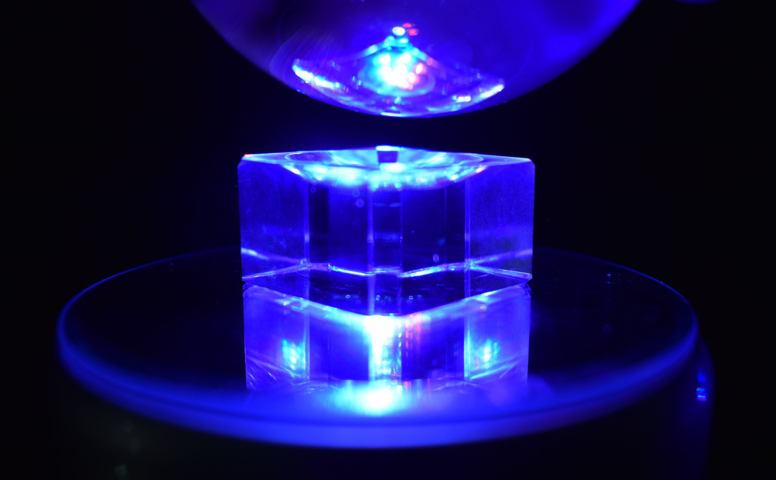 A clear object placed on a mirrored surface, lit from above with a blue light