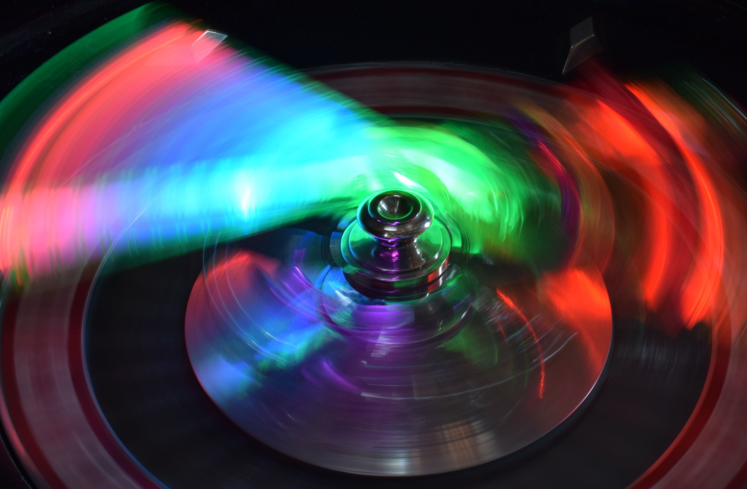 A spinning object is lit by multi-coloured lights, with greens, blues, oranges and purples blending together.