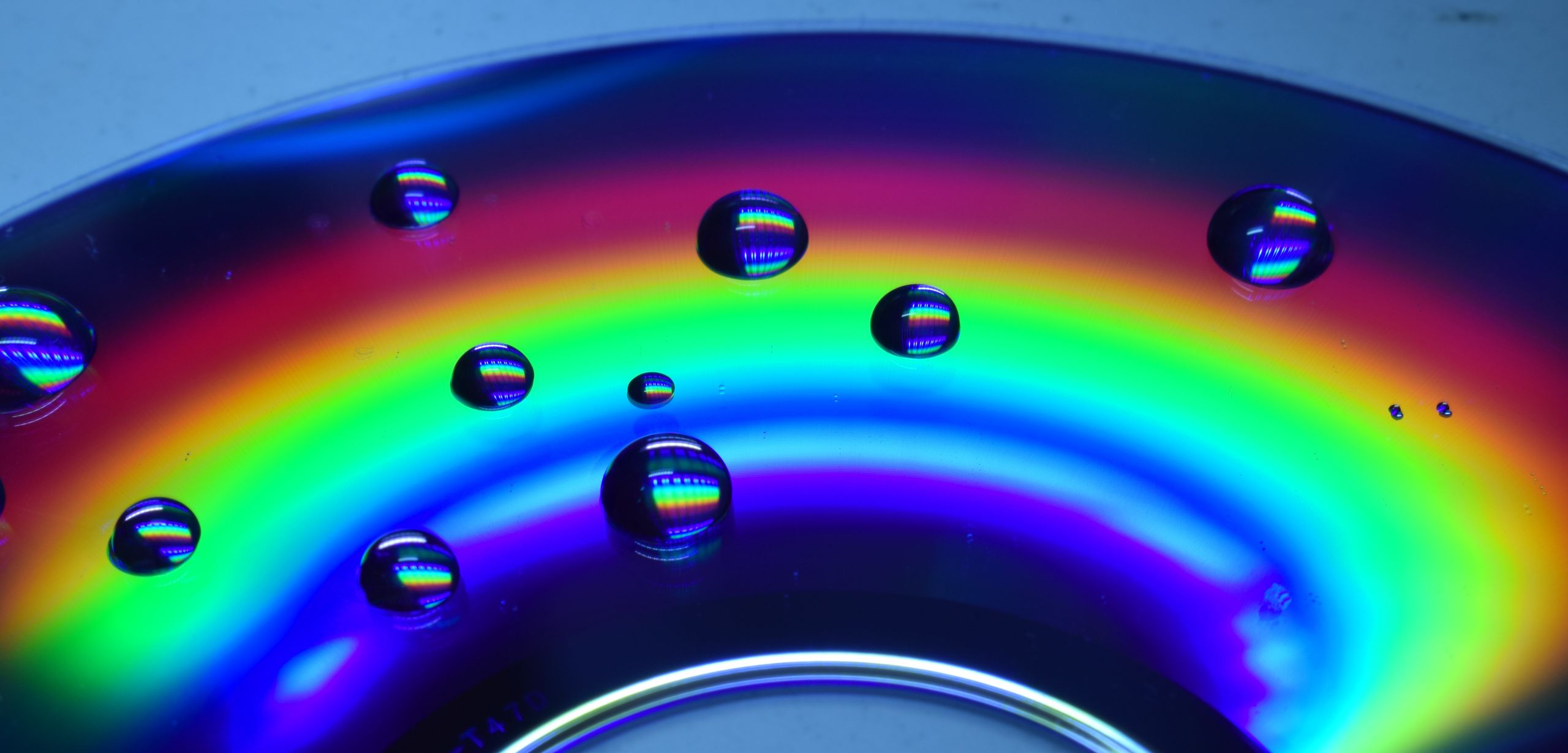 Several water droplets, each reflecting the rainbow of light in the background of the image.